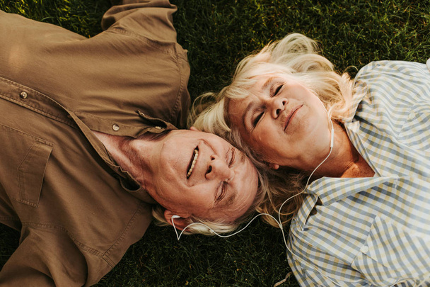 Joyful elderly twosome enjoying music outdoors with smile - Фото, зображення