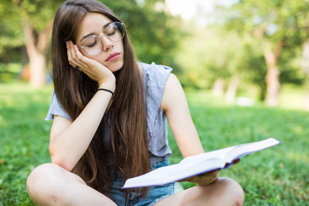 Chica en la hierba en la manta sensación de cansancio al tratar de relajarse al aire libre con libros
 - Foto, imagen