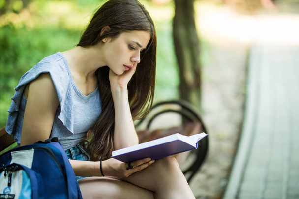 Female student sitting on bench and reading book. - Zdjęcie, obraz