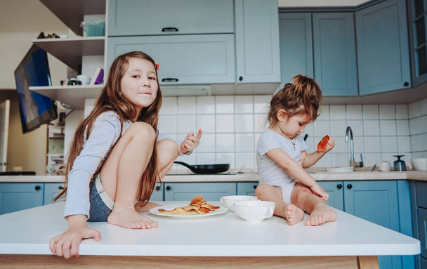 Дві маленькі дівчата на кухні сидять на столі
. - Фото, зображення