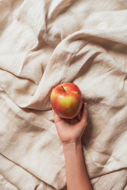 cropped view of woman holding apple on beige sacking cloth - Foto, imagen
