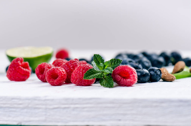 Blueberry, spinachy and orange smoothie on a wooden white background. Glasses of smoothie with berry and mint. Berry, leaf and lime, raspberries on a table. Fruit Healthy food. Breakfast. - Fotografie, Obrázek