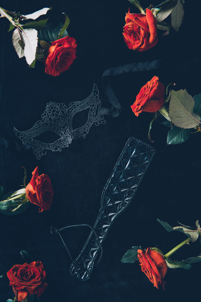 vista superior de la máscara de encaje, paleta de nalgadas de cuero y hermosas rosas rojas en negro
 - Foto, Imagen