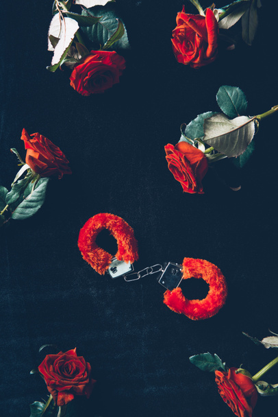 top view of red fluffy handcuffs and beautiful roses on black - Foto, afbeelding