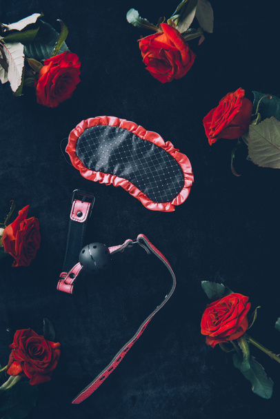 top view of eye mask, gag and red roses on black - Photo, Image