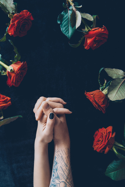 cropped shot of couple holding hands above black fabric with red roses - Foto, Imagem