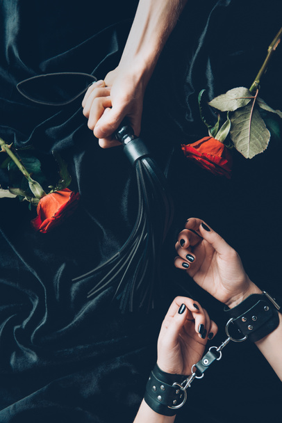 cropped shot of woman in black handcuffs and man holding leather whip - 写真・画像