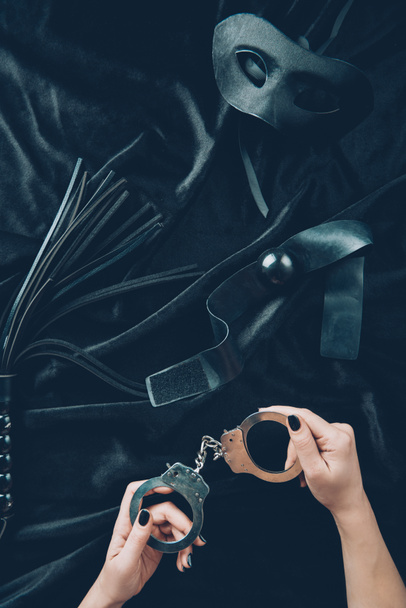 Schnappschuss einer Frau mit Handschellen, Lederpeitsche, Knebel und Maske auf schwarzem Stoff - Foto, Bild