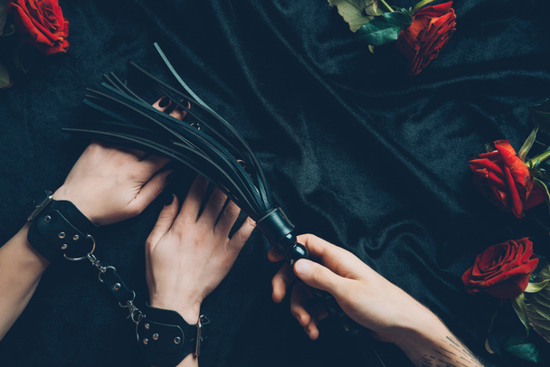 cropped shot of man holding black whip and woman in leather handcuffs - 写真・画像