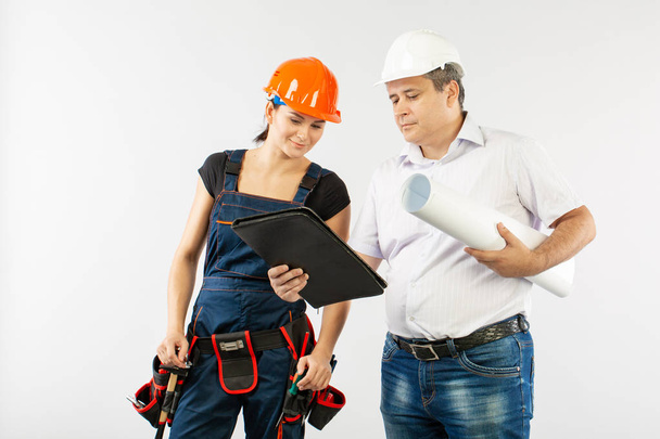 ein Architekt, der einen Hut oder Helm trägt, und eine Bauarbeiterin, die Baupläne überprüft - Foto, Bild