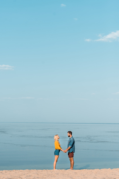 pareja cogida de la mano y mirándose en la playa
 - Foto, imagen