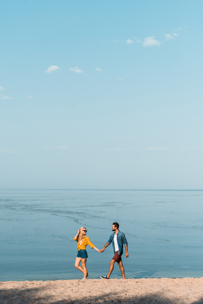 girlfriend and boyfriend holding hands and walking on sandy seashore - Photo, Image