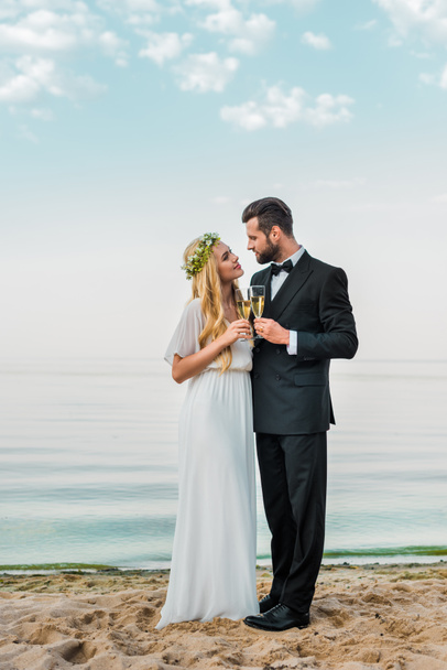 Svatební pár cinkání sklenic šampaňského na pláži a při pohledu na sebe - Fotografie, Obrázek