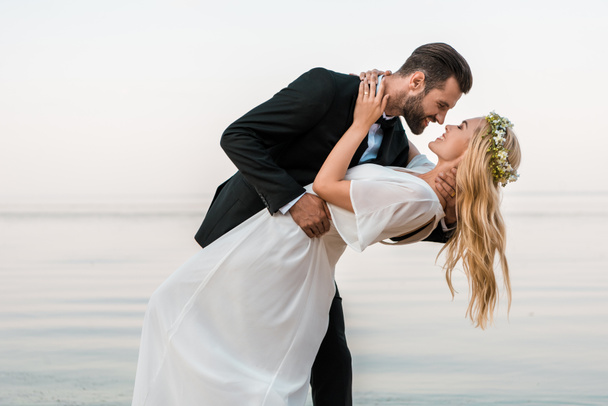 affectionate wedding couple going to kiss on beach - Photo, Image