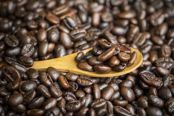 Closeup of fresh roasted coffee beans on the wooden spoon on the table, shot in the studio - 写真・画像