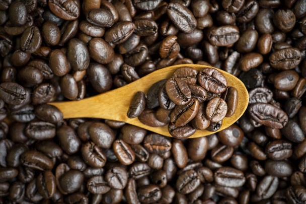 Heap of brown roasted coffee beans with wooden spoon on the table, shot in the studio - Foto, imagen