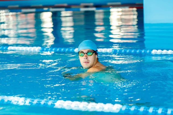 Foto sportovce v modré gumové čepici a brýle při pohledu na fotoaparát v bazénu - Fotografie, Obrázek