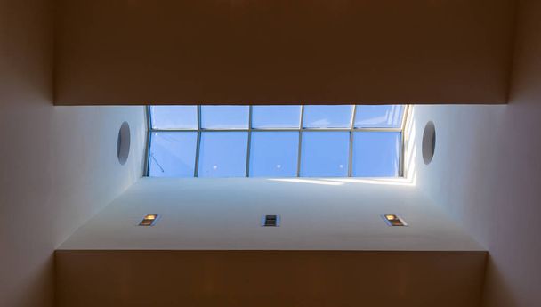 Kijkend naar de blauwe bewolkte hemel door moderne vierkante plafond raam - Foto, afbeelding