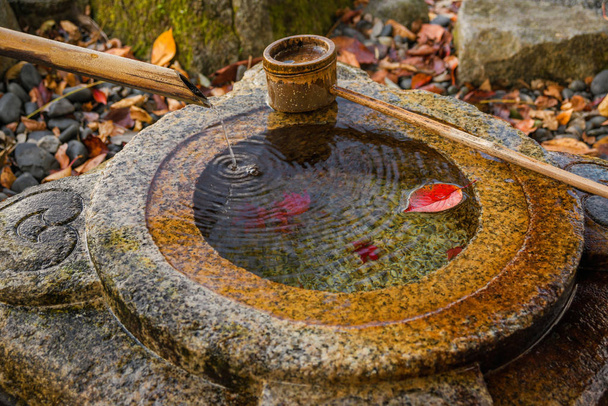 Oude stenen chozubachi voor rituele wassing in Japan, met bamboe pollepel en herfst rood laat binnen - Foto, afbeelding