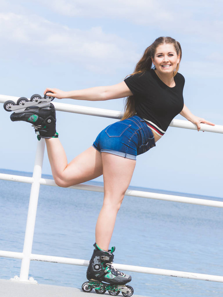 Attractive young woman wearing roller skates relaxing after ride. Fit female having fun during summer time on sea coast. - Zdjęcie, obraz