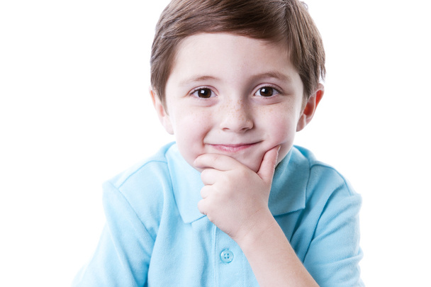 Smiling content caucasian little real boy with his hand on his chin as if he is thinking. - Foto, Imagen