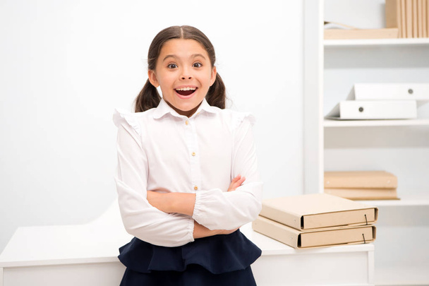 Just heard excellent news. Child girl wears school uniform standing excited face expression. Schoolgirl smart child looks excited white interior background. Girl remember pleasant memory childhood - Foto, Imagen