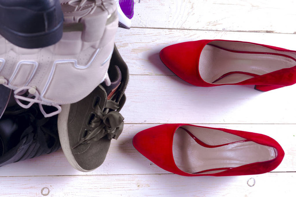 Велика купа різних спортивних взуття і червоне жіноче взуття на високому каблуці на білому тлі
. - Фото, зображення