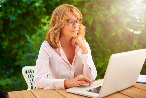 Portrait of concentrating woman sitting behind her laptop and working outside.  - 写真・画像