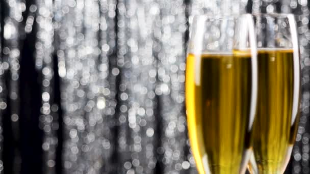 Закрыть два бокала шампанского за праздничным мигающим фоном из мигающей мишуры
. - Кадры, видео