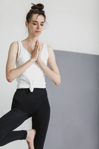 cute graceful girl with long gathered hair in a leotard stands and is engaged in yoga in a bright roo - Photo, Image