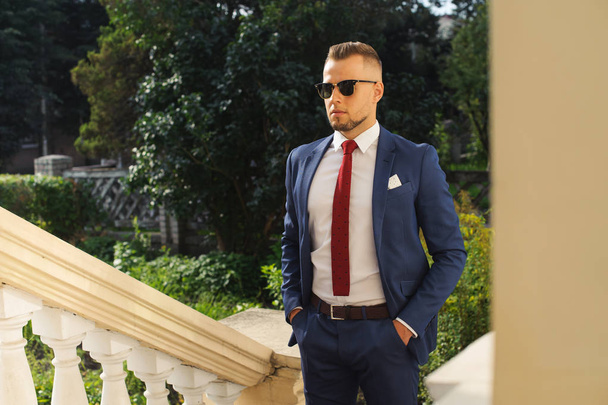 Confident and successful. Beautiful young man in full suit, setting his jacket and looking at the camera while standing in the street - Foto, Imagen