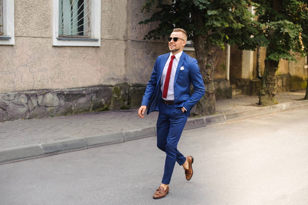 Confidence in every step. The full length of a beautiful young man in full suit adapts his jacket, going forward. - Foto, afbeelding