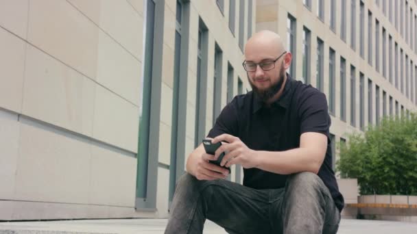 Muž s plnovousem, nosí brýle, pomocí telefonu ve městě - Záběry, video