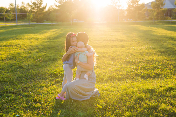 Mooie vrouw met dochter en baby zoon op groen grasveld. Moeder met twee kleine kinderen knuffelen buitenshuis. Gelukkige familie concept - Foto, afbeelding
