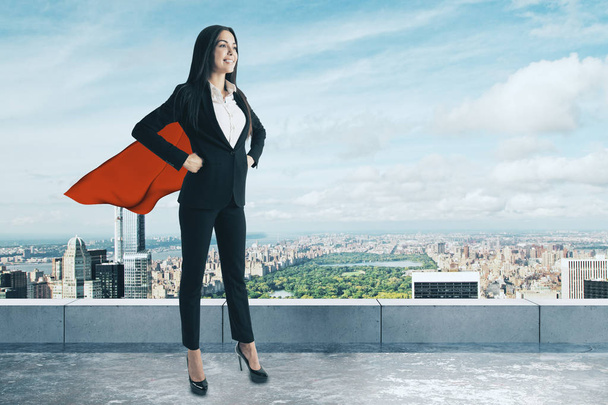 Smiling superhero woman standing on concrete rooftop with city view. Success and leadership concept  - Photo, Image