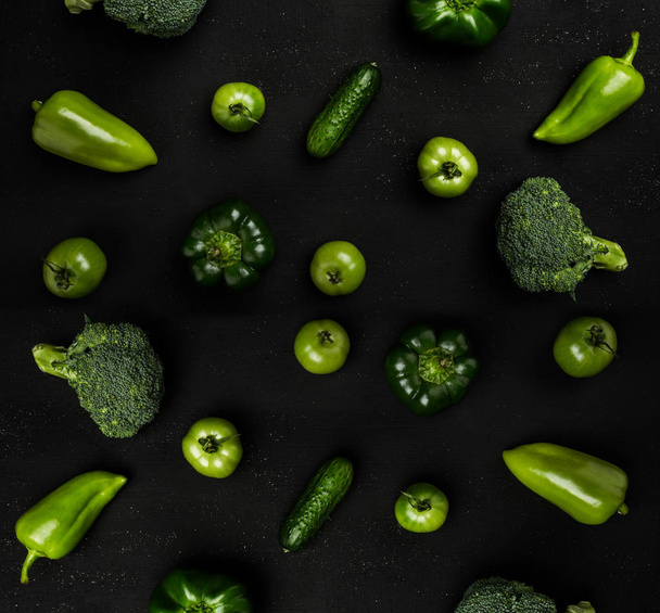 Variety of green vegetables on black table as broccoli, peppers, tomatoes and cucumbers. Top view - Photo, Image