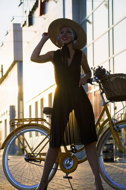 mooi meisje en een fiets die reizen in de stad bij zonsondergang - Foto, afbeelding