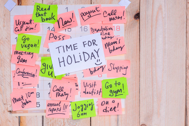 Tempo para férias escrito em nota de papel em um calendário de parede cheio de notas rosa e verde com fundo de madeira e espaço de cópia
 - Foto, Imagem