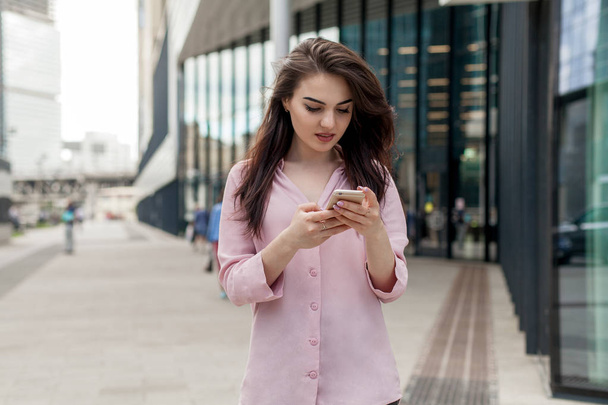 Beautiful brunette girl using online maps in her mobile phone to find the way to a shopping mall. Happy woman browsing smartphone and doing online shopping. Female person texting in cell phone. - Foto, Bild