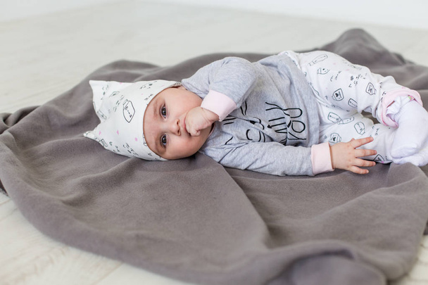 Cute baby lying on a grey blanket and keeps fingers in his mouth. Happy childhood concept. - Fotografie, Obrázek