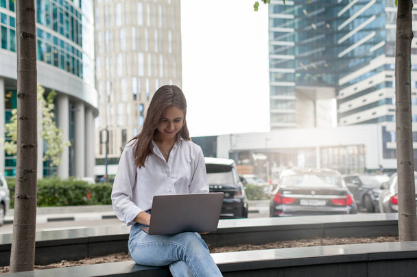 Hübsche Freiberuflerin, die am modernen PC arbeitet, junge Hipstermädchen, die mit Laptop vor ihrem neuen Büro arbeitet, geschäftige Geschäftsfrau, die auf tragbarer Computertastatur tippt und im Internet surft - Foto, Bild