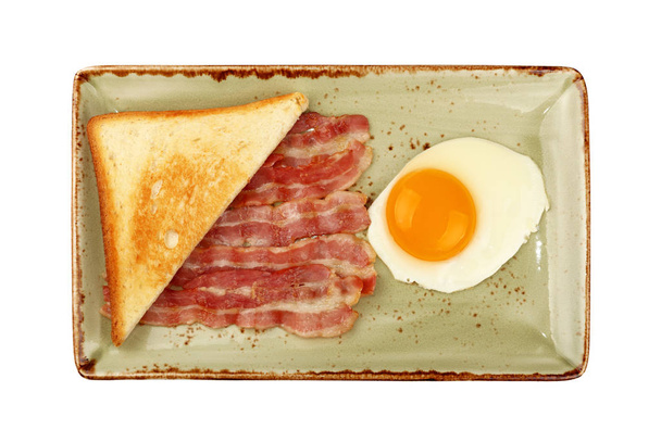 Закрыть английский завтрак, солнечное яйцо, половину поджаренного хлеба и жареный бекон слайсы на голубой тарелке, изолированной на белом фоне, вид сверху, прямо над
 - Фото, изображение