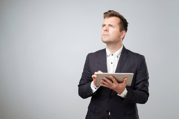 Examining new gadget. Confident young handsome man in suit working on digital tablet while standing against white background. Try to understand how to use new features - Photo, Image