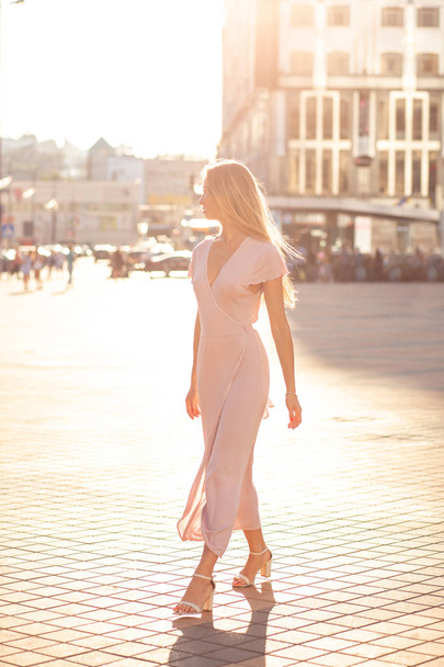 Pretty blonde girl with fluttering hair wearing long knitted dress walking down the street - Photo, Image