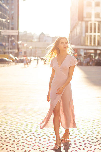 Gorgeous blonde woman with fluttering hair wearing long knitted dress walking down the street - Foto, Imagen