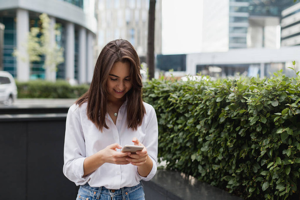 Happy pretty brunette girl business woman using mobile phone, beautiful woman browsing phone and doing online shopping in a mobile app while smiling walking near shopping mall. Online communication. - Foto, Imagem