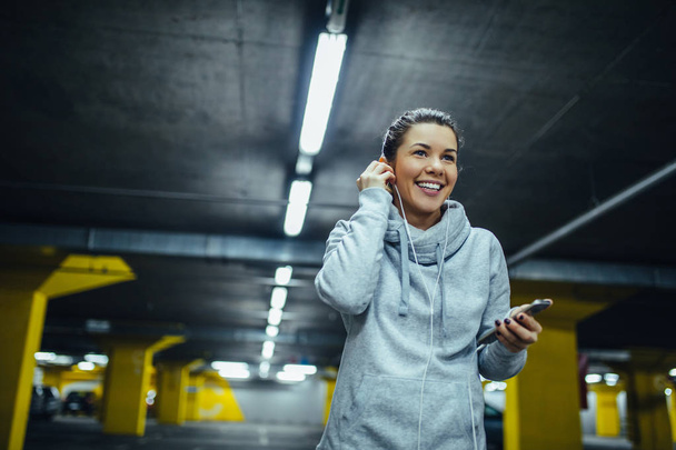Shot of smiling athlete woman putting on earphones during workout. - 写真・画像