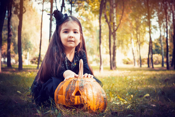 Mädchen im Hexenkostüm mit einem Kürbis im Wald. Hintergrund fröhliche Halloween-Feiertage - Foto, Bild