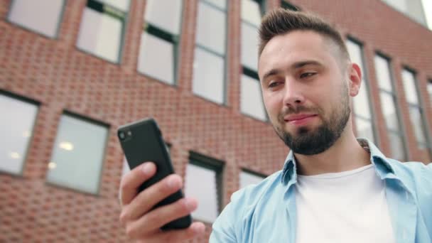 Homem com barba usando um telefone contra um prédio de tijolos
 - Filmagem, Vídeo