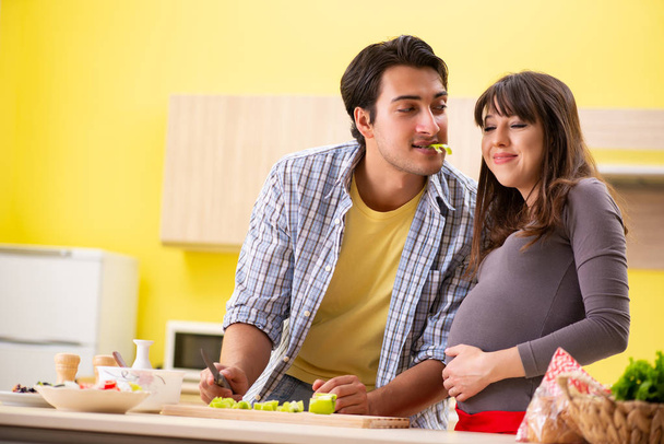 Man and pregnant woman preparing salad in kitchen  - Фото, зображення